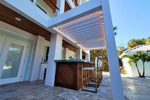 Illuminated Louvered Pergola White louvered pergola with lights over a bar countertop and bar stool